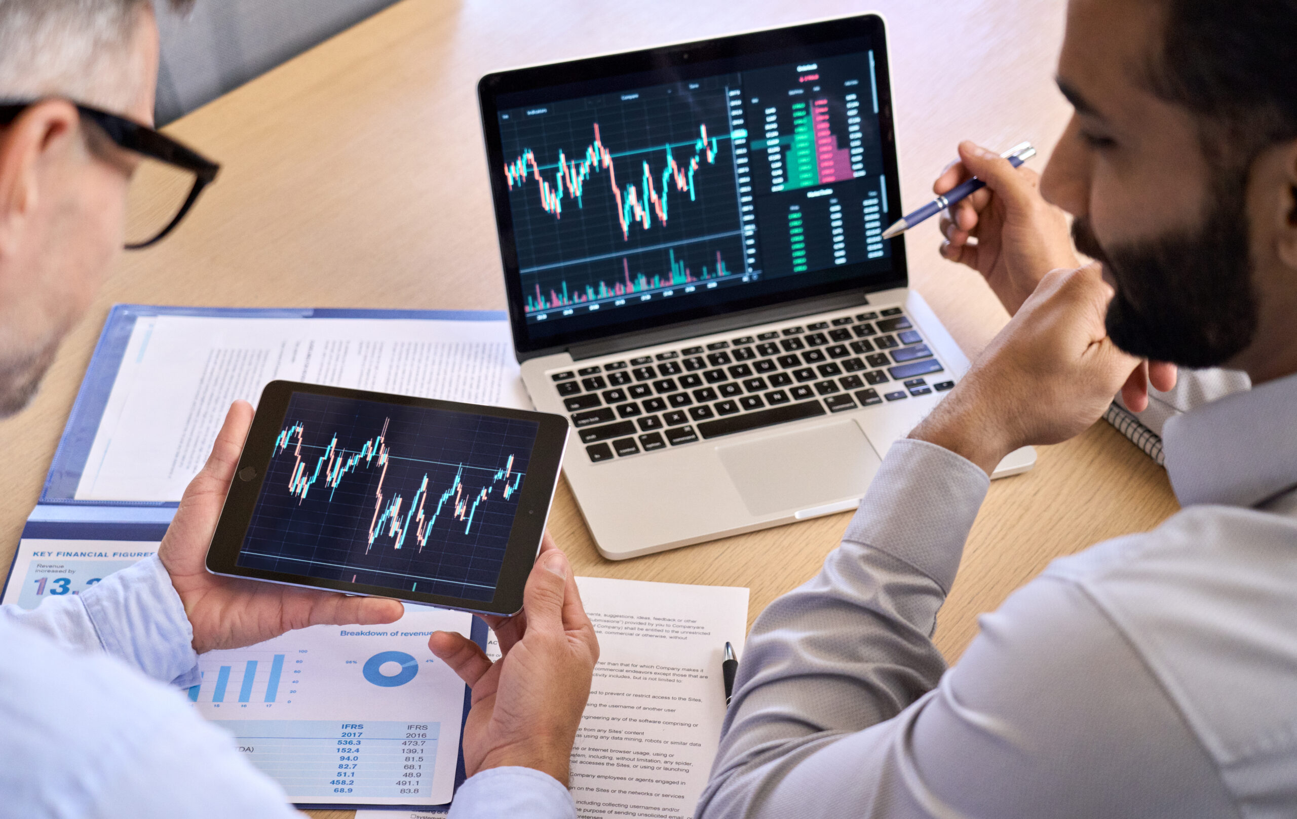Two traders brokers stock exchange investors discussing crypto trading charts. Two diverse traders brokers stock exchange market investors discussing crypto trading charts growth using digital tablet and laptop analyzing financial risks, investment profit, global rates forecast.